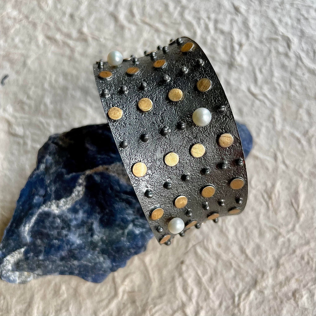 The newest addition to Mia Siya - An oxidized plated over brass bracelet cuff that so gracefully showcases artistic gold dots in addition to pearls, lavishly distributed alongside. A mild stretch would make the wear comfortable!