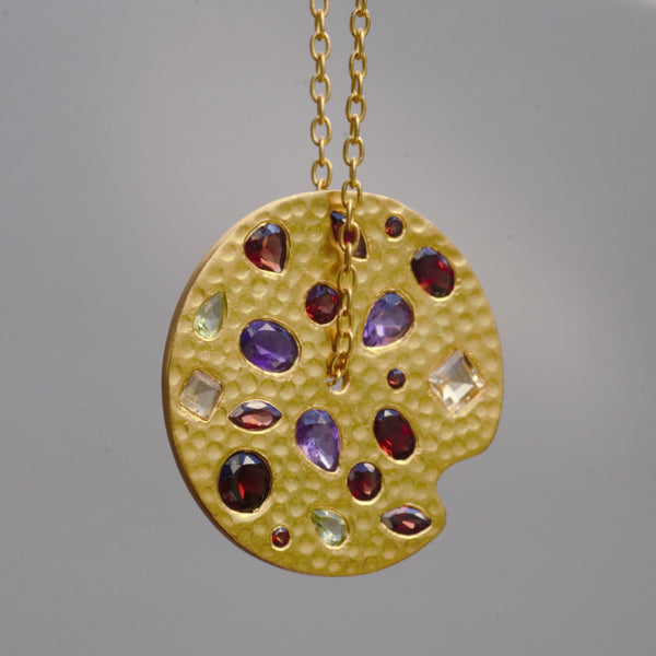 A unique gold plated medallion, rather than a painter's palette with embedded gemstones such as amethyst, garnet, black onyx, and prehnite is simply eye-catching.