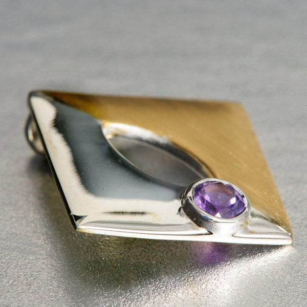 A square-shaped, but when worn it looks more of a diamond-shaped pendant is, two toned-sterling silver on one side and sterling silver with gold plating on the other side. It has a 4mm amethyst gemstone which is embedded with perfection and finesse