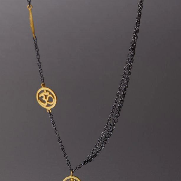 A spiritually inclined design where one side of the necklace holds cute little, gold plated 'OM' charms and on the other side are 3 plain chains. The necklace then holds yet another sleek, handcrafted 'OM' charm as a pendant. The necklace is a sterling silver base with black rhodium plating.