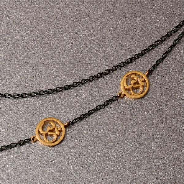 A spiritually inclined design where one side of the necklace holds cute little, gold plated 'OM' charms and on the other side are 3 plain chains. The necklace then holds yet another sleek, handcrafted 'OM' charm as a pendant. The necklace is a sterling silver base with black rhodium plating.